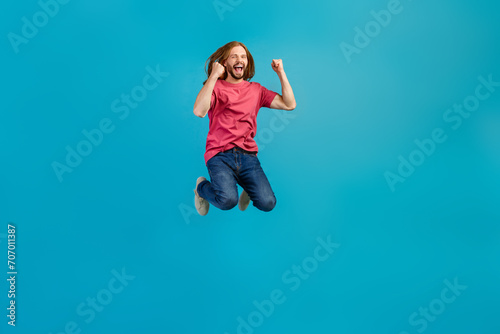 Full body photo of overjoyed energetic person raise fists jumping empty space isolated on blue color background