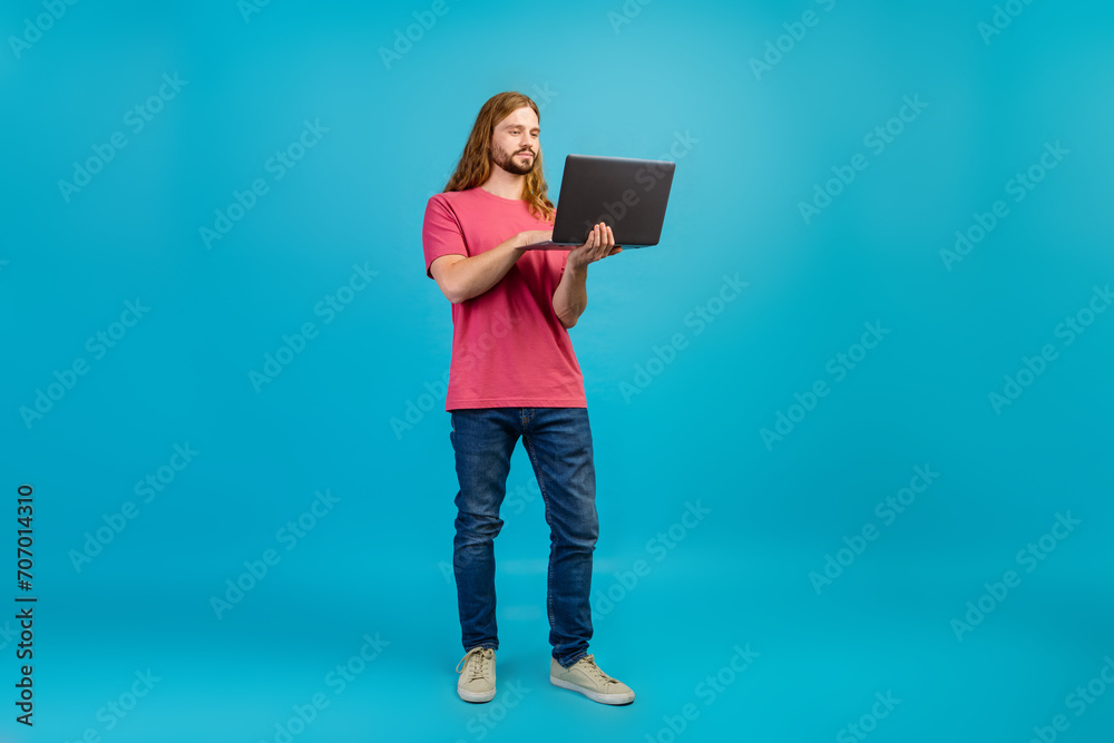 Full length photo of nice young man hold use wireless netbook empty space isolated on blue color background Full length photo of nice young man hold use wireless netbook empty space isolated on blue color background