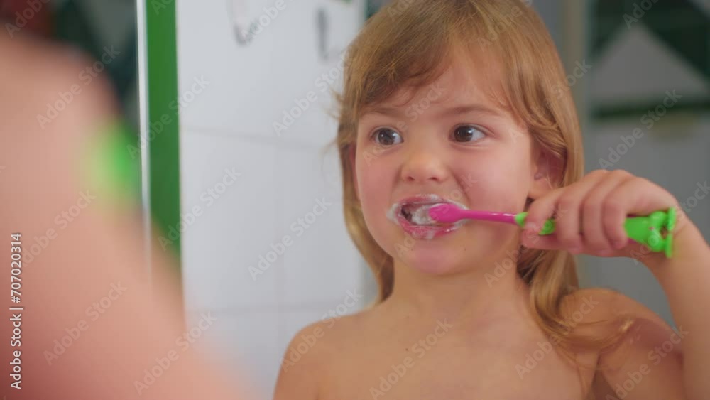Cute little girl brushing teeth her toothbrush looking at mirror. Children daily health care routine. Close-up Cute little girl brushing teeth her toothbrush looking at mirror. Children daily health care routine. Close-up