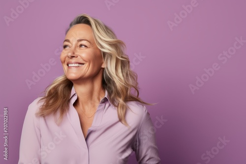 Portrait of happy mature businesswoman smiling and looking away against purple background.