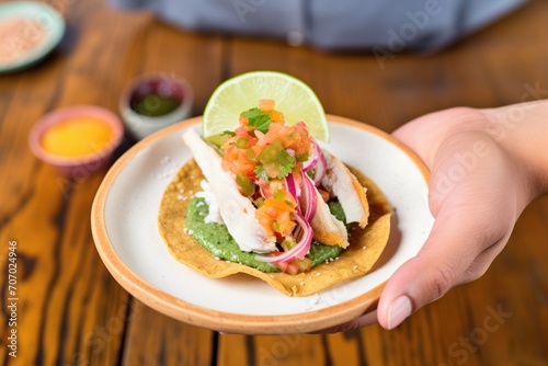 hand holding a tostada topped with fish ceviche and hot sauce