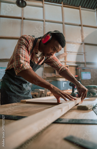 African male lines up piece of wood while working on carpentry project in woodwork warehouse 