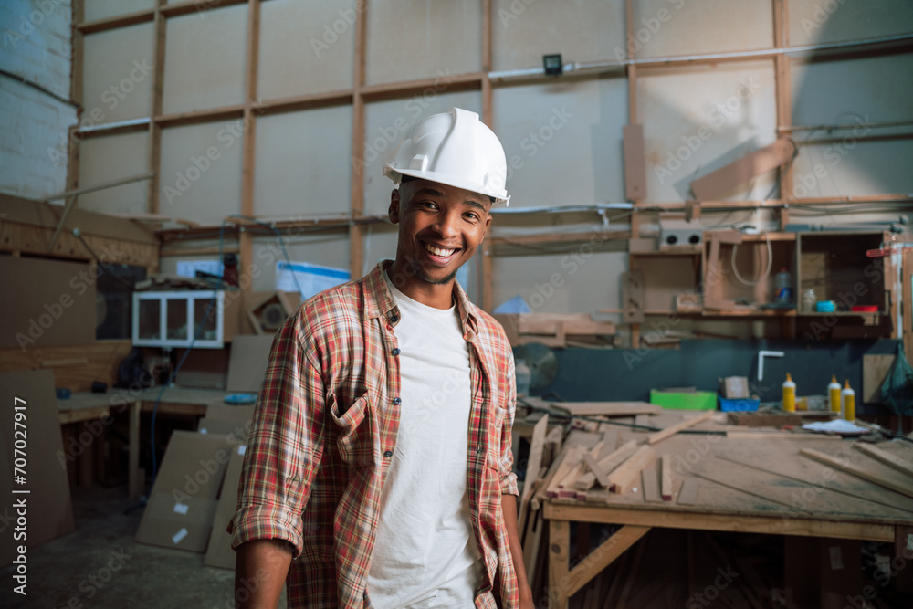 Happy African American male with hardhat stands in carpentry factory Happy African American male with hardhat stands in carpentry factory