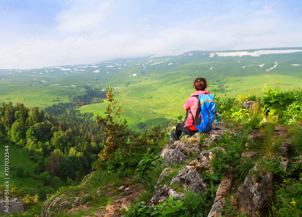 Hiker with backpack relaxing on top of a mountain and enjoying valley view
