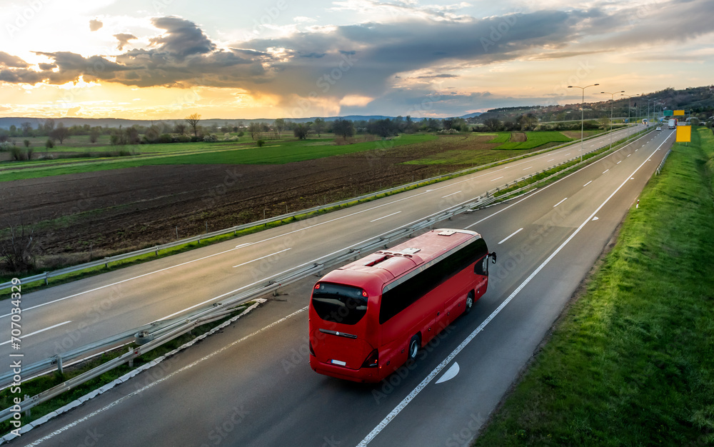 Red Modern comfortable tourist bus driving through highway at bright sunny sunset. Travel and coach tourism concept. Trip and journey by vehicle