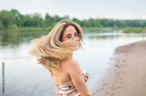 glückliche junge Frau mit wehenden Haaren steht am Fluss © luna