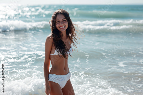 young beautiful smiling girls in a white swimsuit is standing on the beach among the sea waves