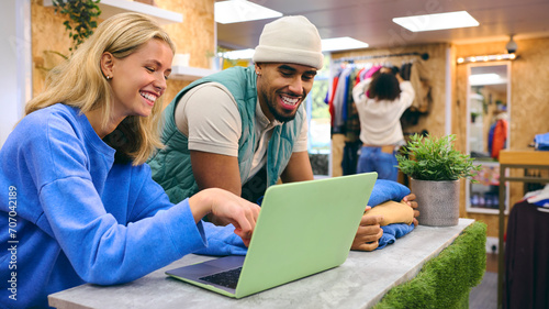 Male And Female Sales Assistant Working At Cash Desk With Laptop In Pop Up Fashion Or Clothes Store