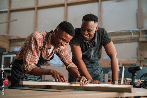 African American male measures piece of wood as colleague assists him in carpentry workshop