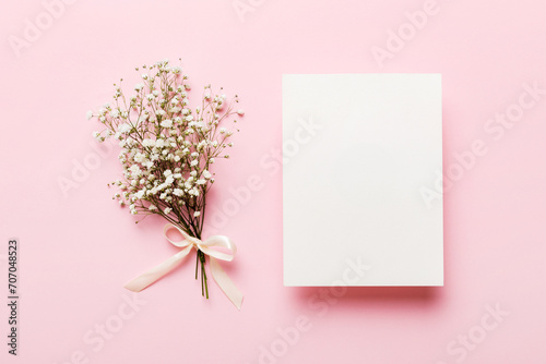 Wedding mockup with white paper list and flowers gypsophila on colored table top view flat lay. Blank greeting cards and envelopes. Beautiful floral pattern. Flat lay style photo