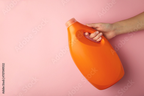 Hand with liquid laundry detergent bottle, cleaning soap for cloth on pink background. Space for text photo