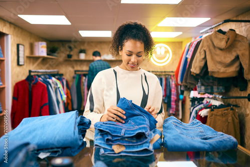 Female Sales Assistant Or Customer Sorting And Looking At Stock Of Jeans In Fashion Or Clothes Store photo