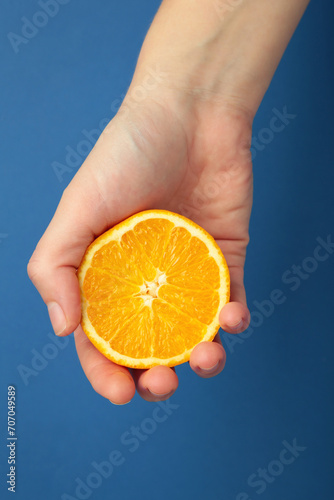 Female hand squeezing half of orange on blue background. Vertical photo