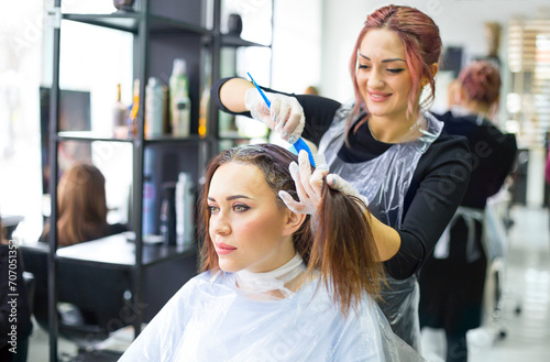 Professional female hairdresser applying color to female customer at design hair salon, woman having her hair dyed