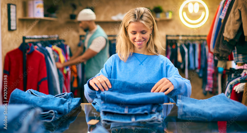 Female Sales Assistant Or Customer Sorting And Looking At Jeans In Fashion Store