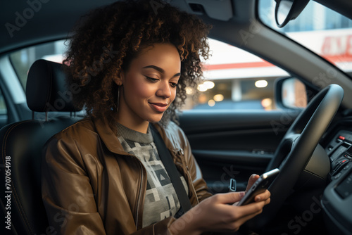 Beautiful African-American woman driving a car looks at the smartphone screen.