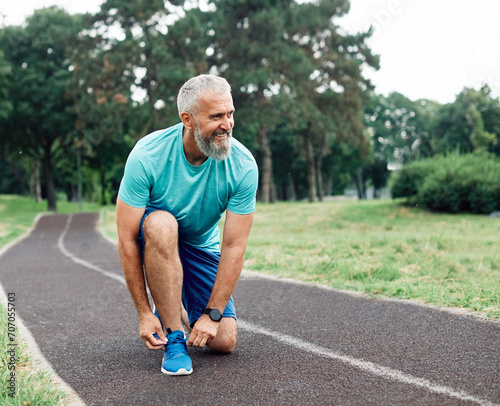 Portrait of a happy active mature or middle aged senior man posing fixing shoelace on his running shoe after exercising outdoors, vitality and active senior concept
