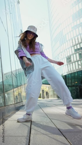 Fashionable funky caucasian girl dancer in sportswear is performing outdoor street dancing motion . slow motion video. Joyful summer female artist demonstrate choreography in the city.