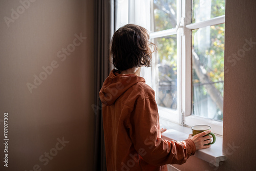 Quadro su tela Woman looking at window drinking tea coffee on kitchen at home enjoying pastime leisure, rear view