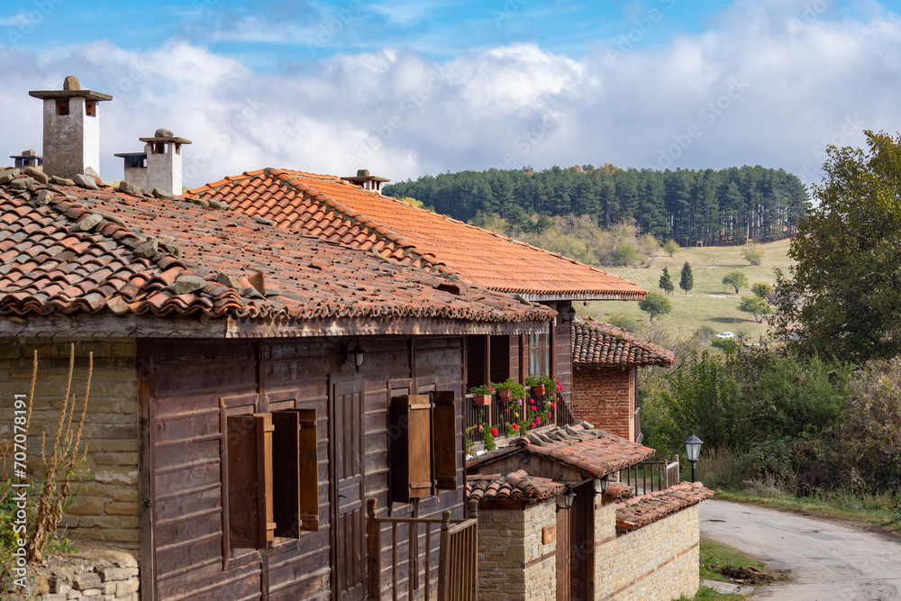 Old time traditional rural house with wooden walls and windows, stone fence with gate on the street, landscape. Typical architecture from the Bulgarian National Revival period. Historical place, Kotel Old time traditional rural house with wooden walls and windows, stone fence with gate on the street, landscape. Typical architecture from the Bulgarian National Revival period. Historical place, Kotel