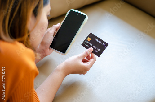 Asian woman holding black credit card lying on sofa