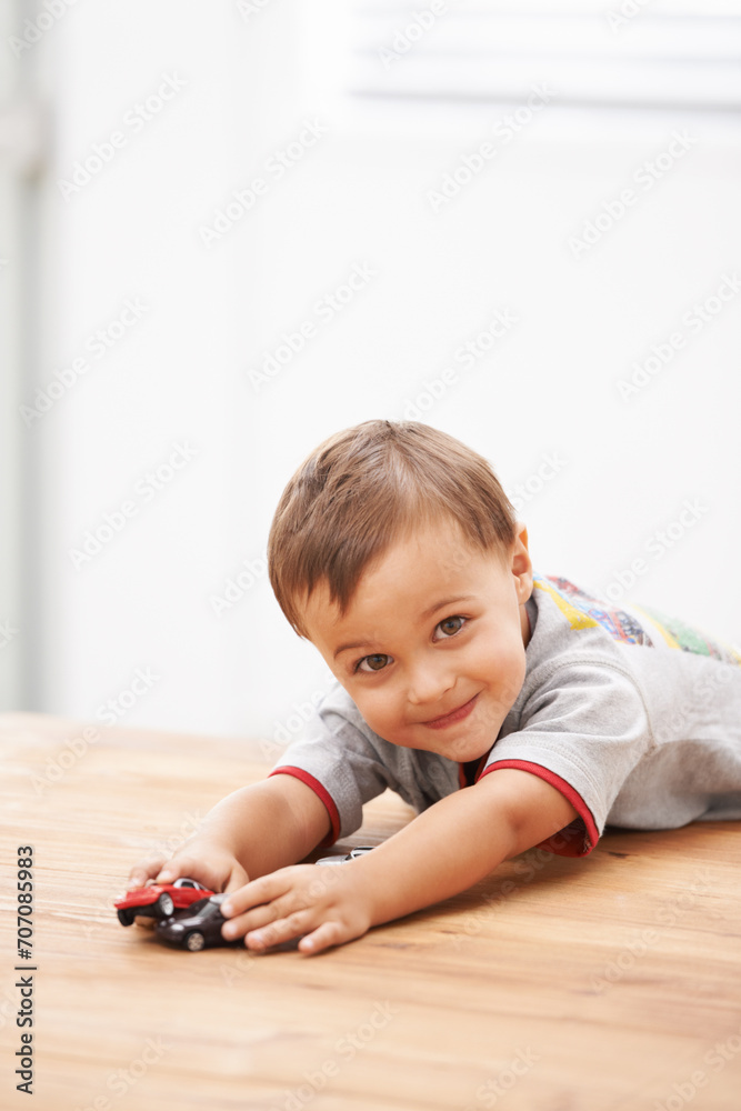 Naklejka premium Cars, toys and portrait of child by table playing for learning, development and fun at modern home. Cute, sweet and boy kid enjoying a game with plastic vehicles by wood for childhood hobby at house.