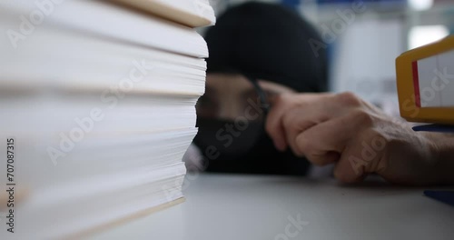 Person in balaclava with magnifying glass looks at documents in office. Industrial business espionage and intellectual property theft concept photo