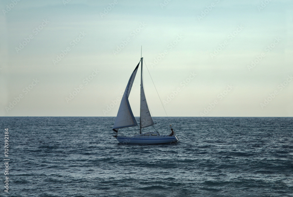 Sunset on the open sea and in the distance the silhouette of a person sitting on a lonely small sailboat