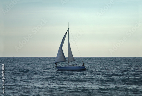 Sunset on the open sea and in the distance the silhouette of a person sitting on a lonely small sailboat