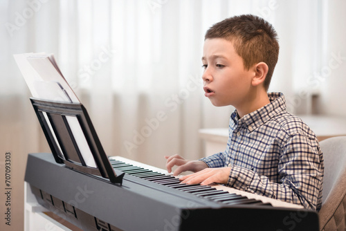 Little Boy Child Leaning to Play the Piano by Notes. Piano Lessons for Schoolboy. Focused  Pupil Playing Piano with Notes. photo