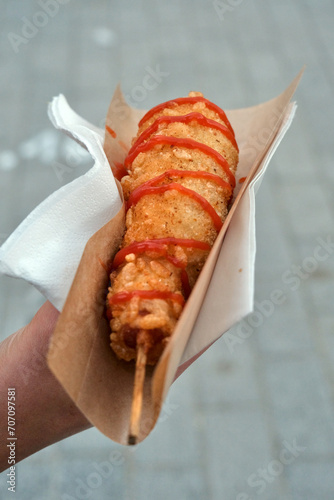 Korean gamja hot dog, with a dash of ketchup, held in a napkin photo