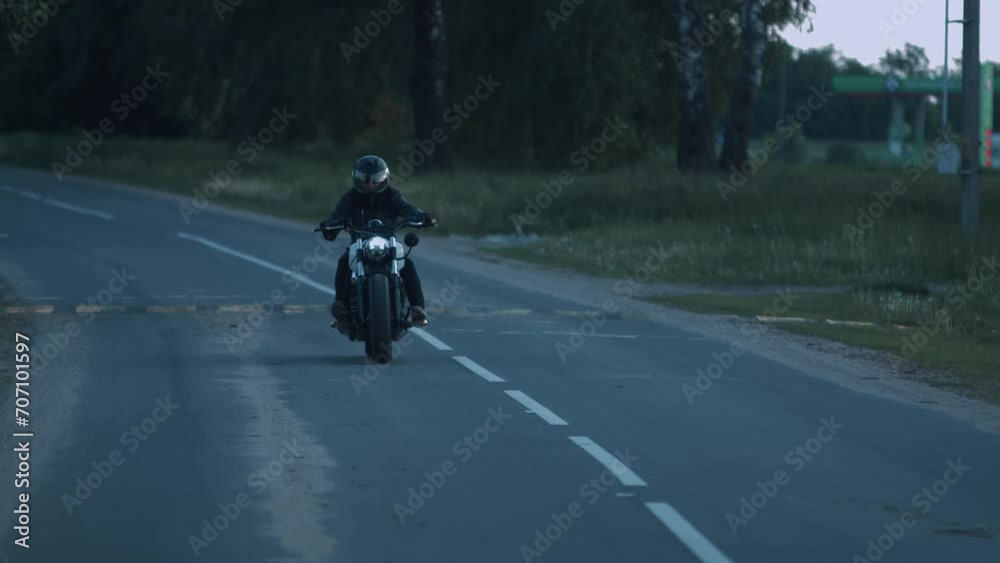 Man in black helmet and in black clothes rides motorcycle with headlight on along suburban highway. Slow motion Man in black helmet and in black clothes rides motorcycle with headlight on along suburban highway. Slow motion