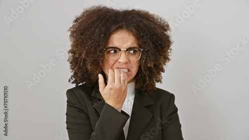 Anxious hispanic woman with curly hair looking worried, biting nails, overwhelmed by stress, standing against a stark white isolated background. photo