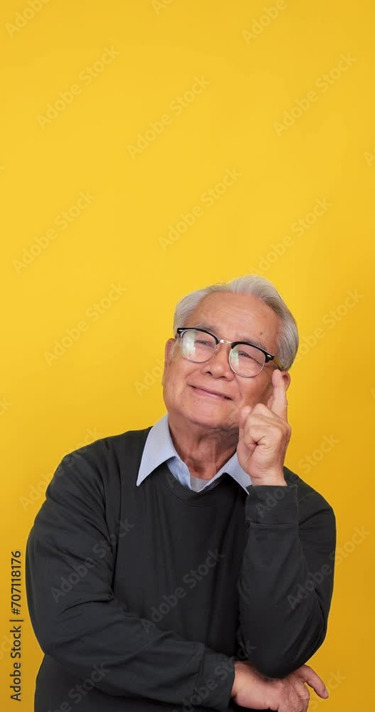 Vertical clip. An old Asian man is thinking and deciding something. Isolated on yellow background in the studio. Vertical clip. An old Asian man is thinking and deciding something. Isolated on yellow background in the studio.