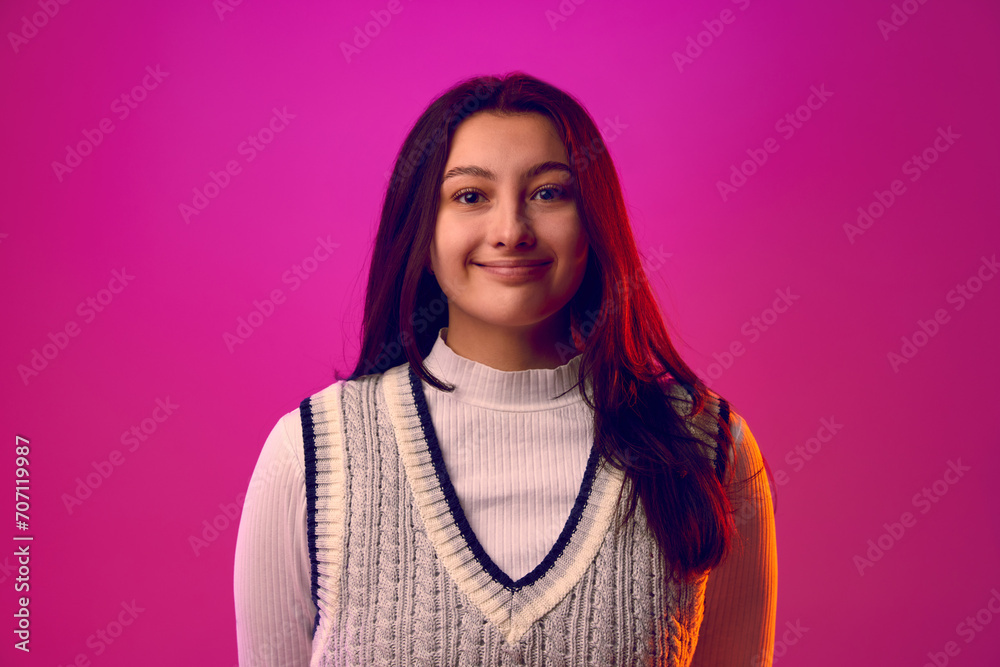 Fototapeta premium Young woman with long brunette hair, dressed casual outfit smiling looking at camera against gradient pink background. Concept of human emotions, self-expression, fashion and style. Ad