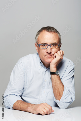 Bored, portrait and senior businessman in a studio with pride for legal corporate career. Glasses, table and professional elderly male lawyer with tired face expression isolated by gray background.
