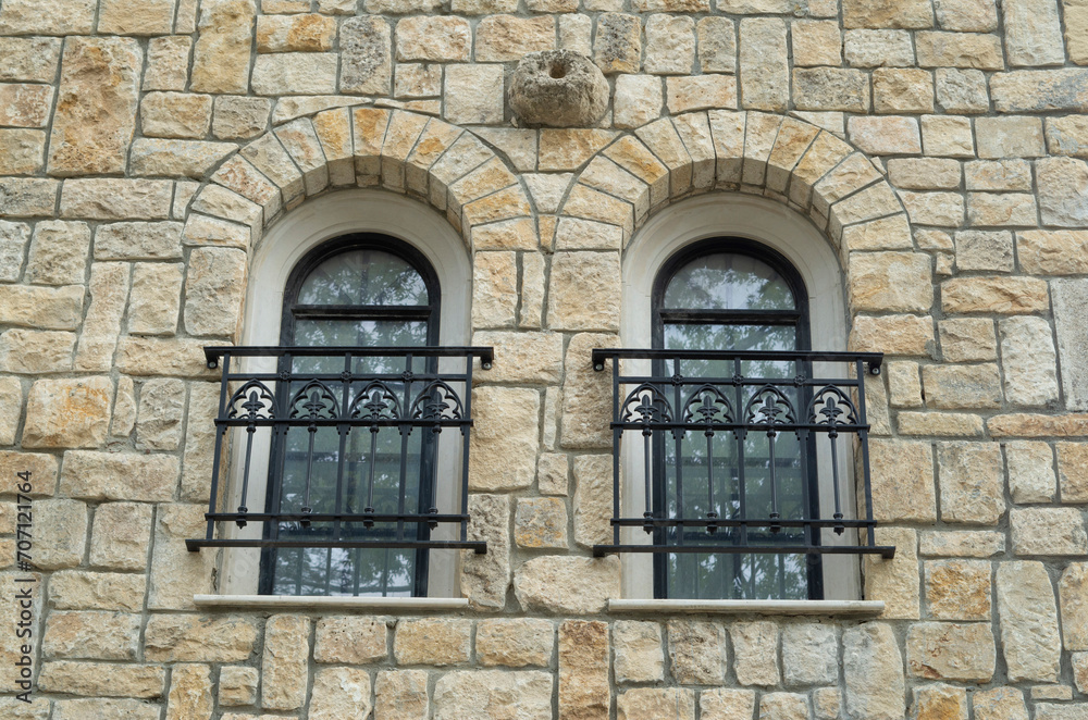 Two arched windows with black wrought iron window railings on stone wall Two arched windows with black wrought iron window railings on stone wall