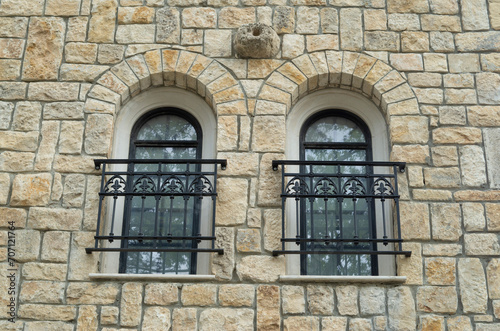 Two arched windows  with black wrought iron window railings on stone wall