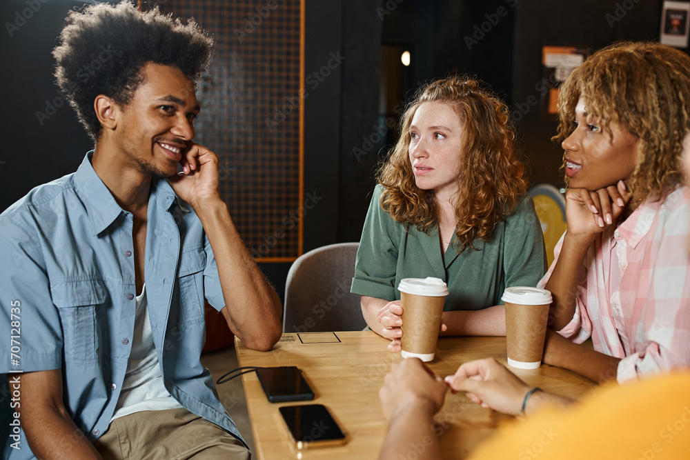 smiling and stylish african american man talking to multicultural friends in cafe of students hostel
