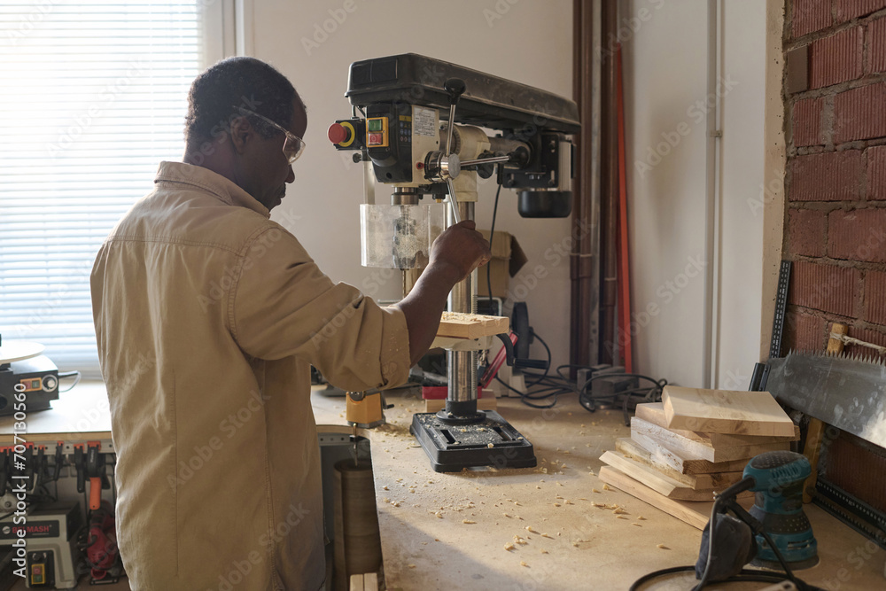 Black male carpenter using wood cutting machines in workshop working on home improvement project