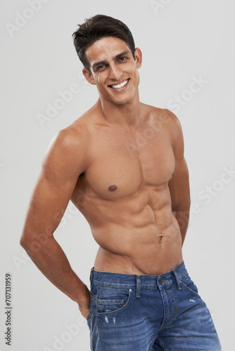 Man, portrait and happy in studio for fashion, confidence and bodybuilder in jeans for style. Male person, shirtless and fitness or muscle progress, face and body care or wellness by gray background