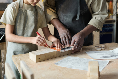 Closeup of unrecognizable carpenter teaching little girl woodworking in crafts school for children