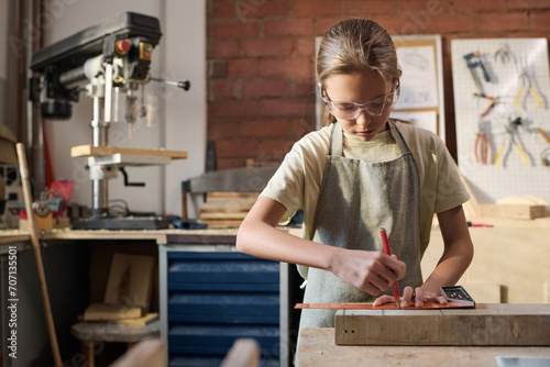 Waist up portrait of Caucasian girl measuring wooden board and building model in carpenting workshop photo