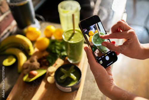 Woman taking photo of a green smoothie with fresh ingredients on kitchen counter photo