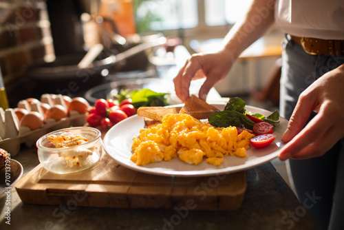 Woman serving scrambled eggs with toast and fresh tomatoes on a plate for breakfast photo