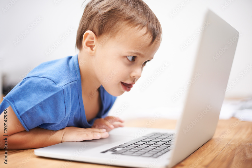 Boy child, laptop and reading in home with search, movies and cartoon with learning video for development. Kid, computer and watch at desk in family house for education, studying and online course Boy child, laptop and reading in home with search, movies and cartoon with learning video for development. Kid, computer and watch at desk in family house for education, studying and online course