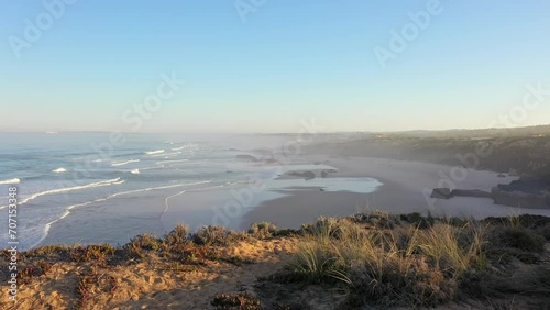 Aerial view of Praia do Malhao beach at sunrise with fog and haze in Portugal. flying over the shore of a rocky abyss