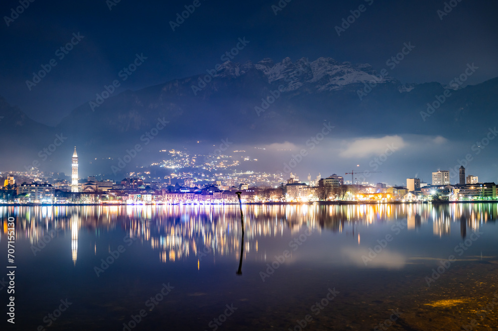 The city of Lecco, with its lakeside promenade and its buildings, photographed in the evening in winter.