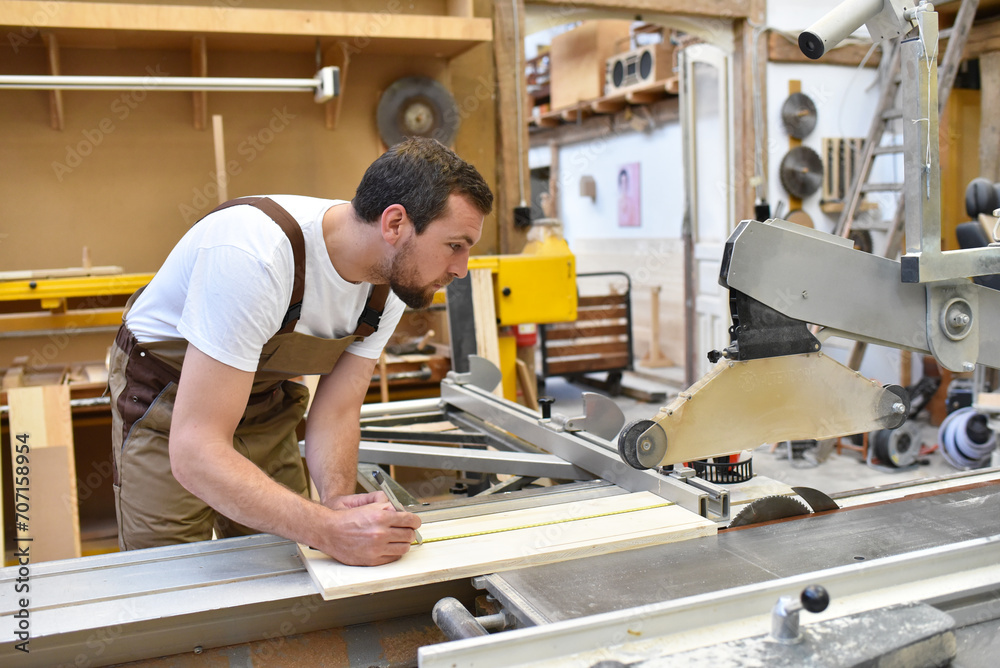 friendly carpenter with ear protectors and working clothes working on a saw in the workshop friendly carpenter with ear protectors and working clothes working on a saw in the workshop