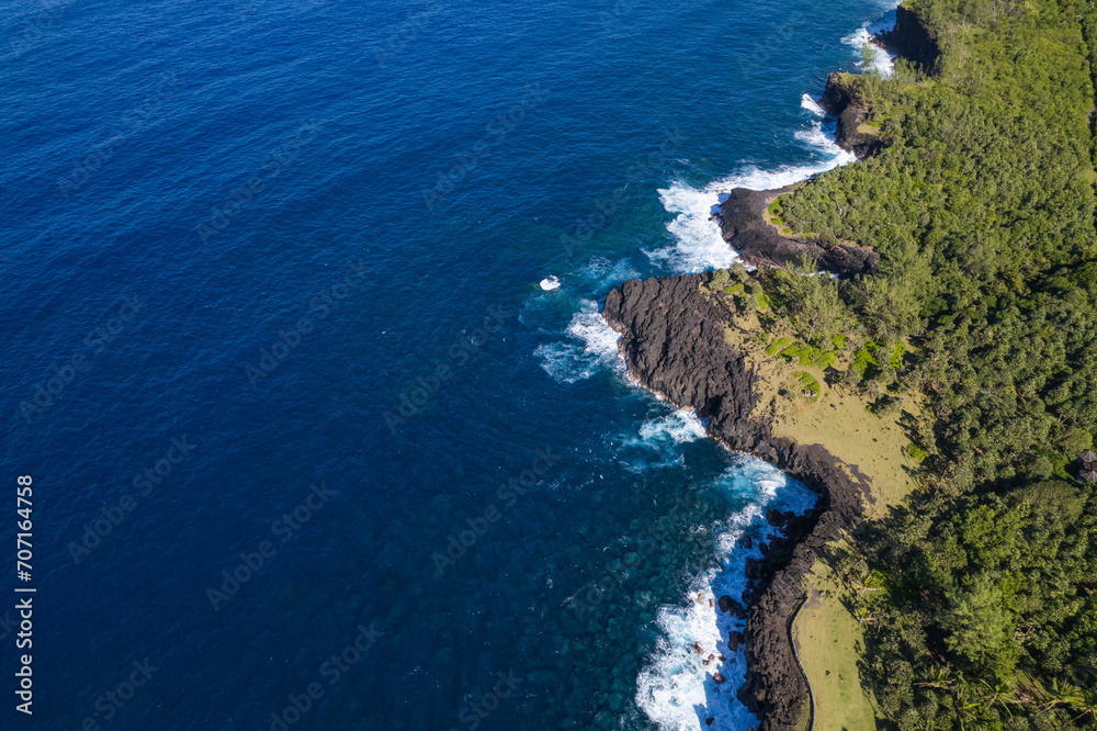 Aerial view of the black lava cliffs formed by the different flows that threw themselves into the blue of the ocean, of Cap Méchant, the sea and its palm forest, Reunion Island Aerial view of the black lava cliffs formed by the different flows that threw themselves into the blue of the ocean, of Cap Méchant, the sea and its palm forest, Reunion Island